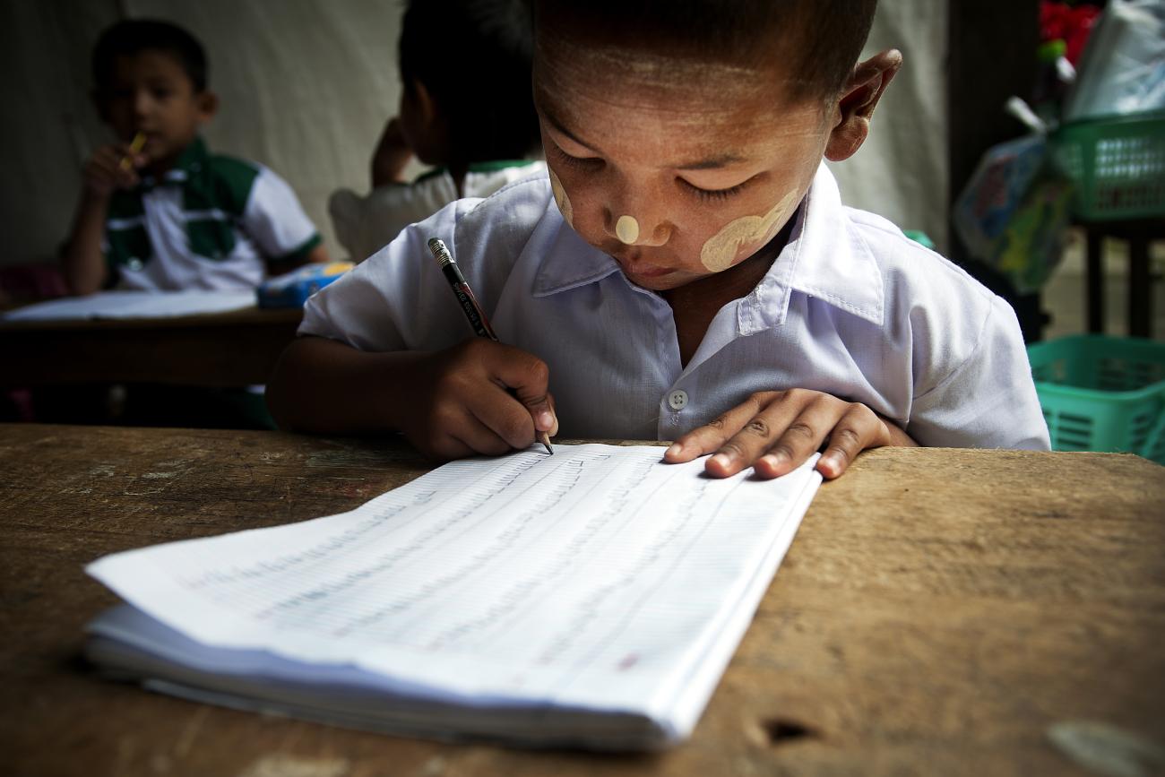 تُظهر لافتة عدم ترك أي أحد خلف الركب طفلاً يتدرب على الكتابة أثناء فصل روضة الأطفال في تاشيلك، ميانمار