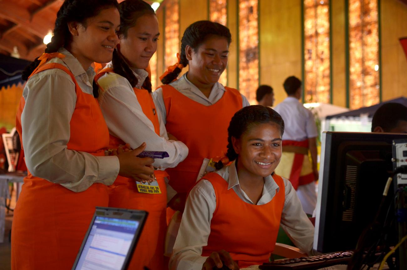Des jeunes filles portant un uniforme de couleur orange travaillent sur un ordinateur en souriant.
