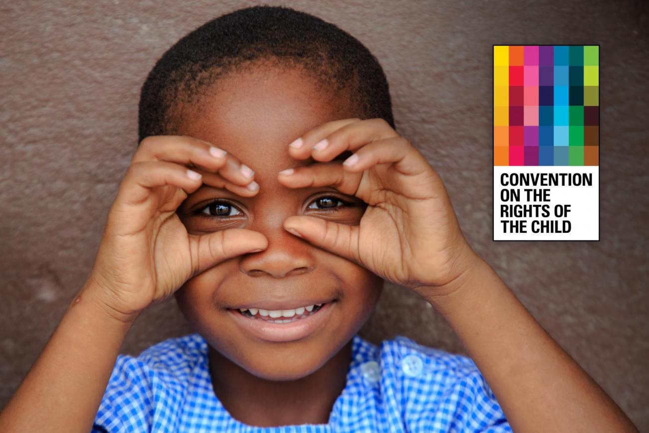 The image shows a cheerful child with their hands serving as binoculars with the cover of the Convention on the Rights of the Child publication.