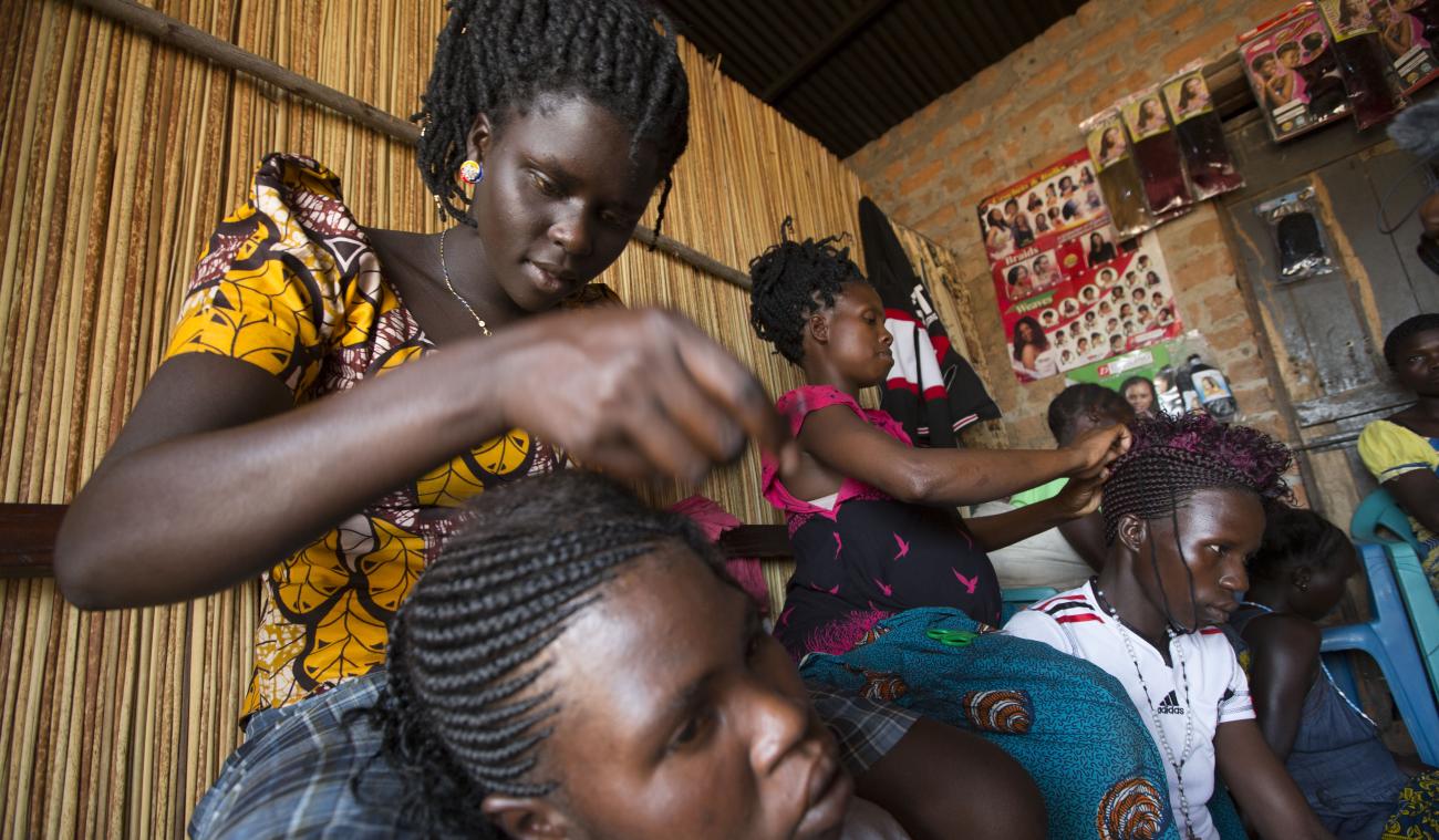 A Ugandan woman plaiting her customer's hair at a beauty salon.