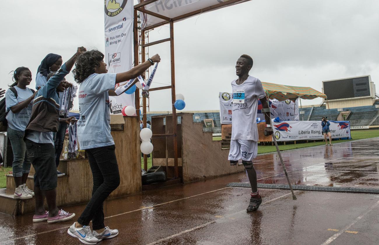 Los simpatizantes aplauden al primer participante discapacitado con muletas en cruzar la línea de meta de la parte de 10 kilómetros del Maratón de Liberia.