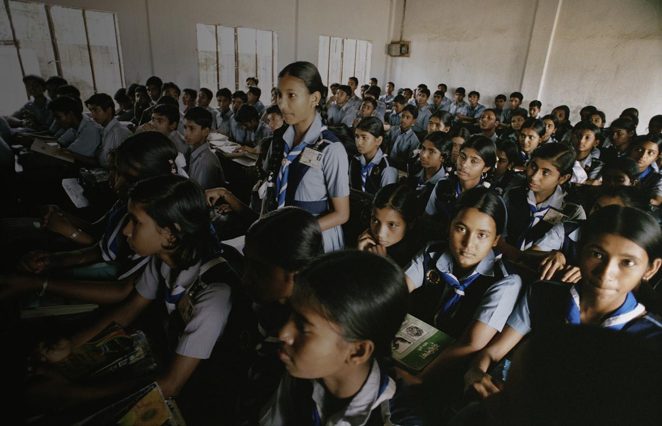 Une jeune fille se tient debout au milieu d'autres élèves, dans une salle de classe, pour répondre à une question.