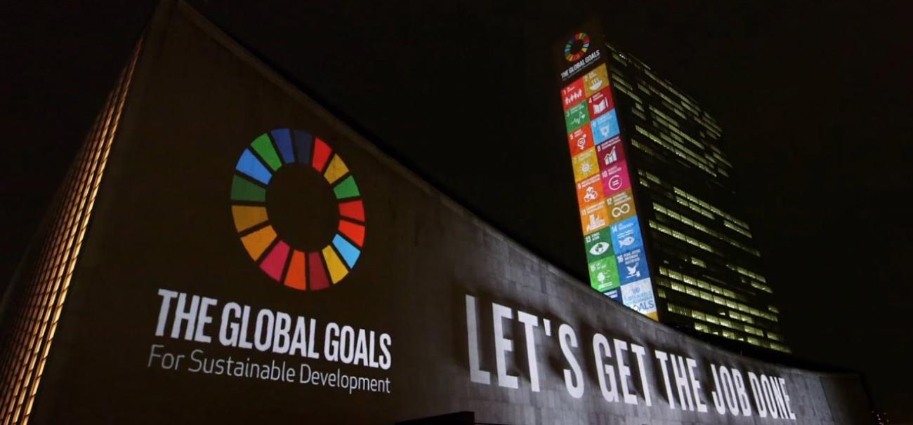The UN Building at night showing projected images of the SDGs and text saying "Let's Get the Job Done". 