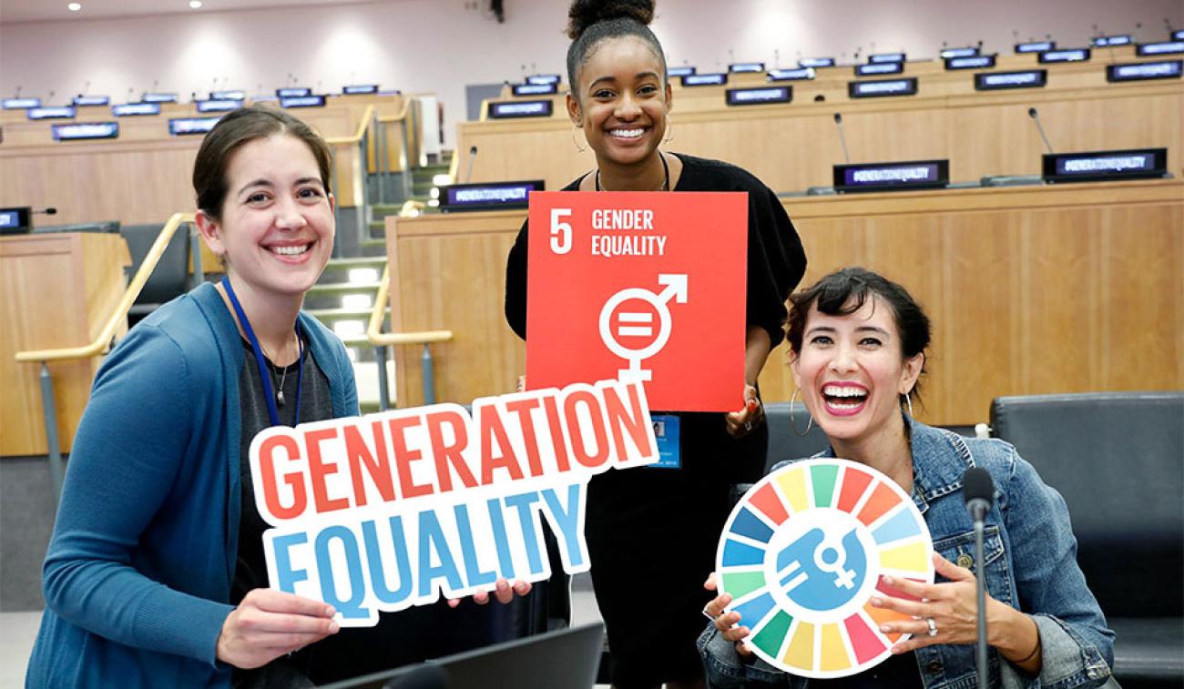 Tres jóvenes sostienen el cartel de los ODS y de la generación igualdad.