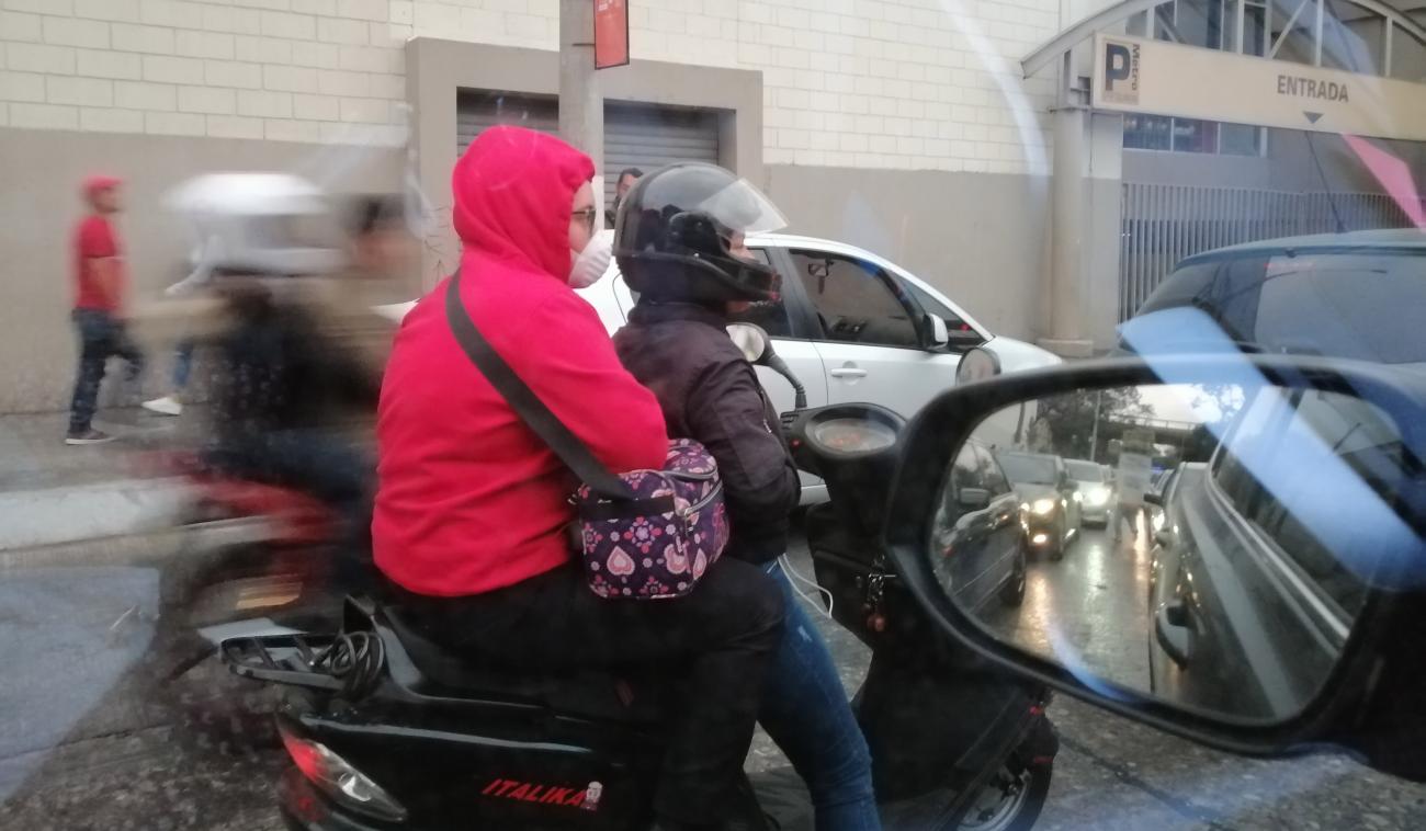 View of two people riding a motorbike wearing protective masks.