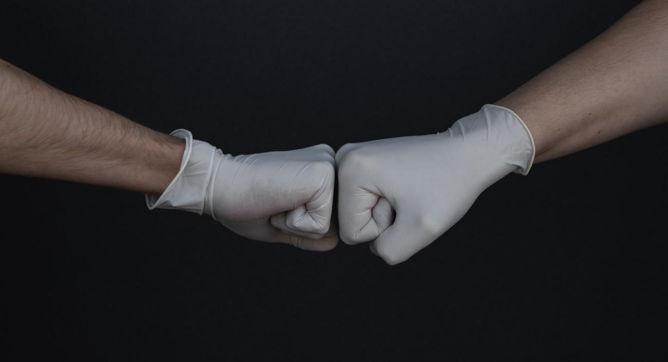 Two hands wearing gloves are shown fist bumping against a solid black background.