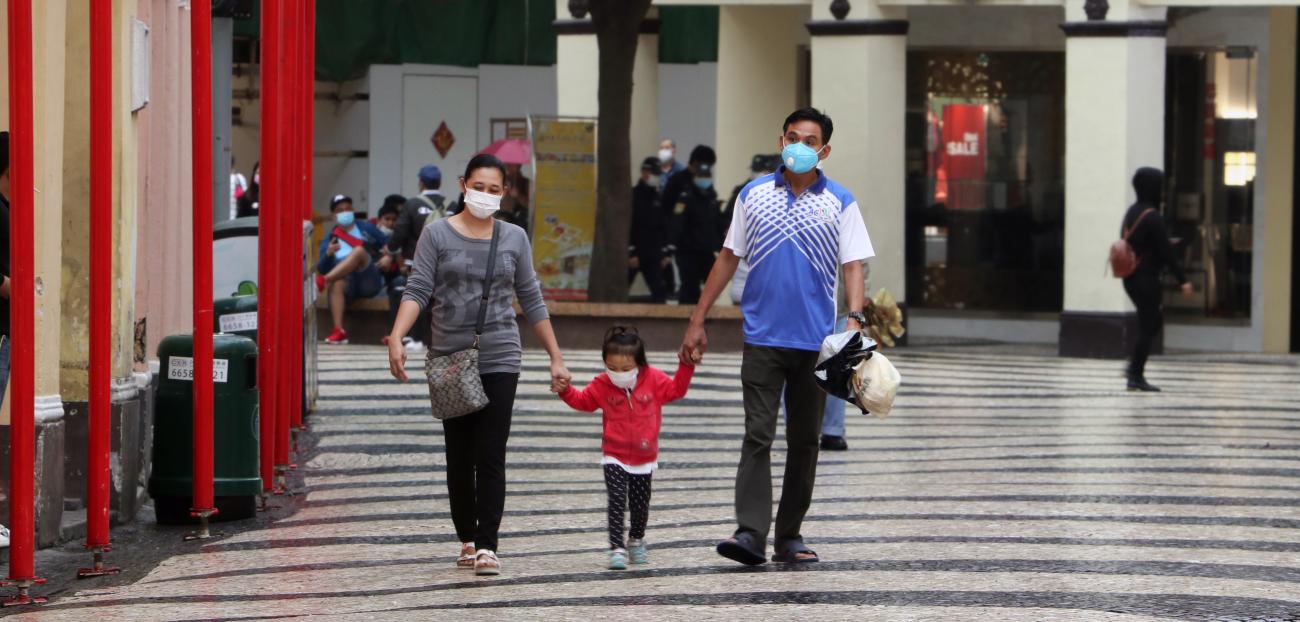 Mother, father and child hold hands as they walk together at a shopping centre, wearing protective face masks.