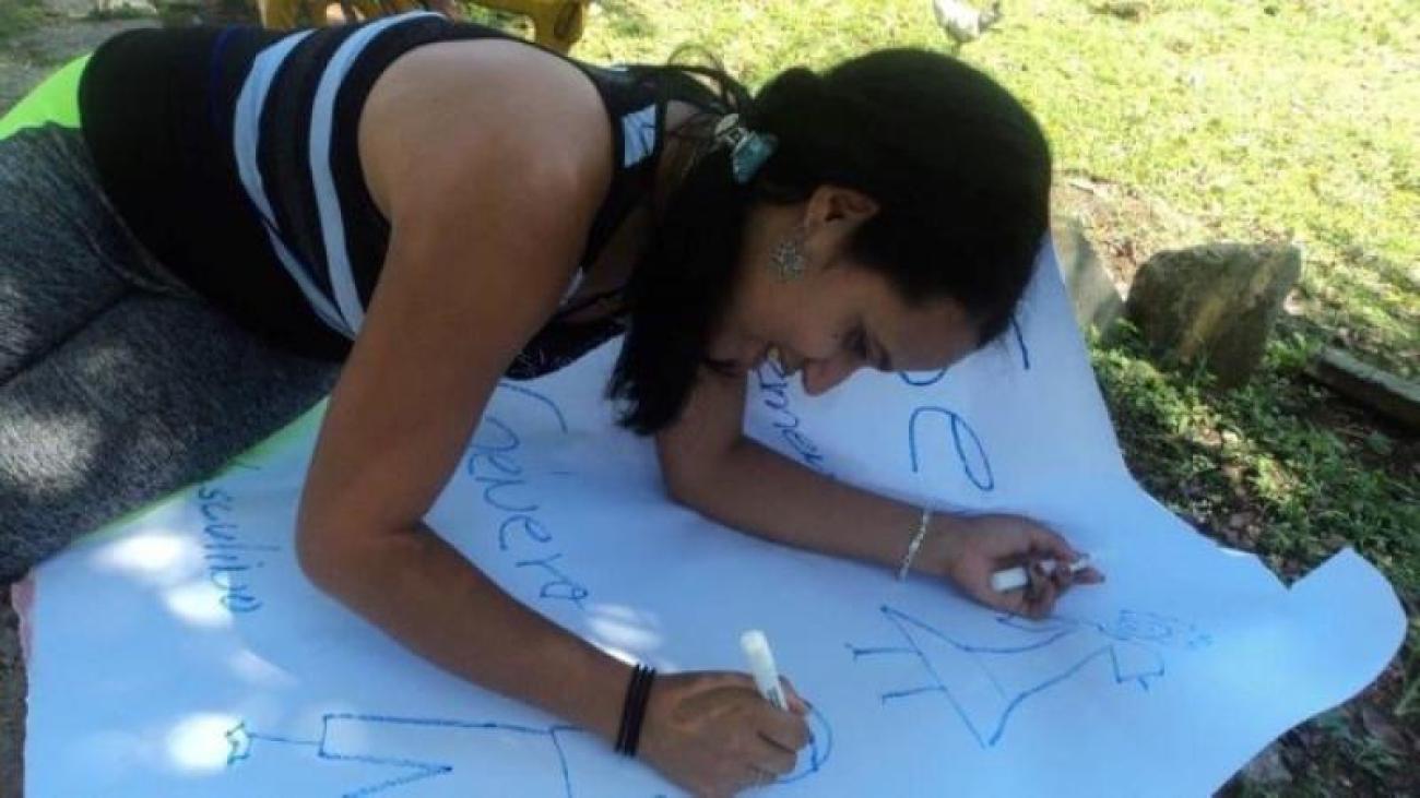 Une jeune femme est assise dans l’herbe et écrit sur une grande feuille de papier en souriant.