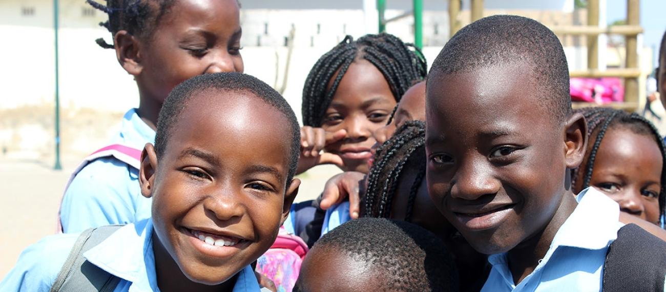 Close up of children from Beira, one of Mozambique’s largest cities, happily smile at the camera in front of a playground.