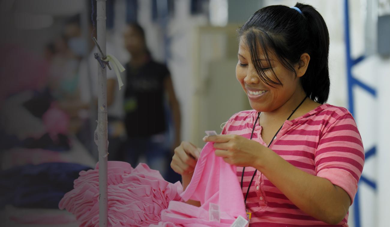 在尼加拉瓜的一家服装厂，一名服装工人在换班时微笑着缝制。