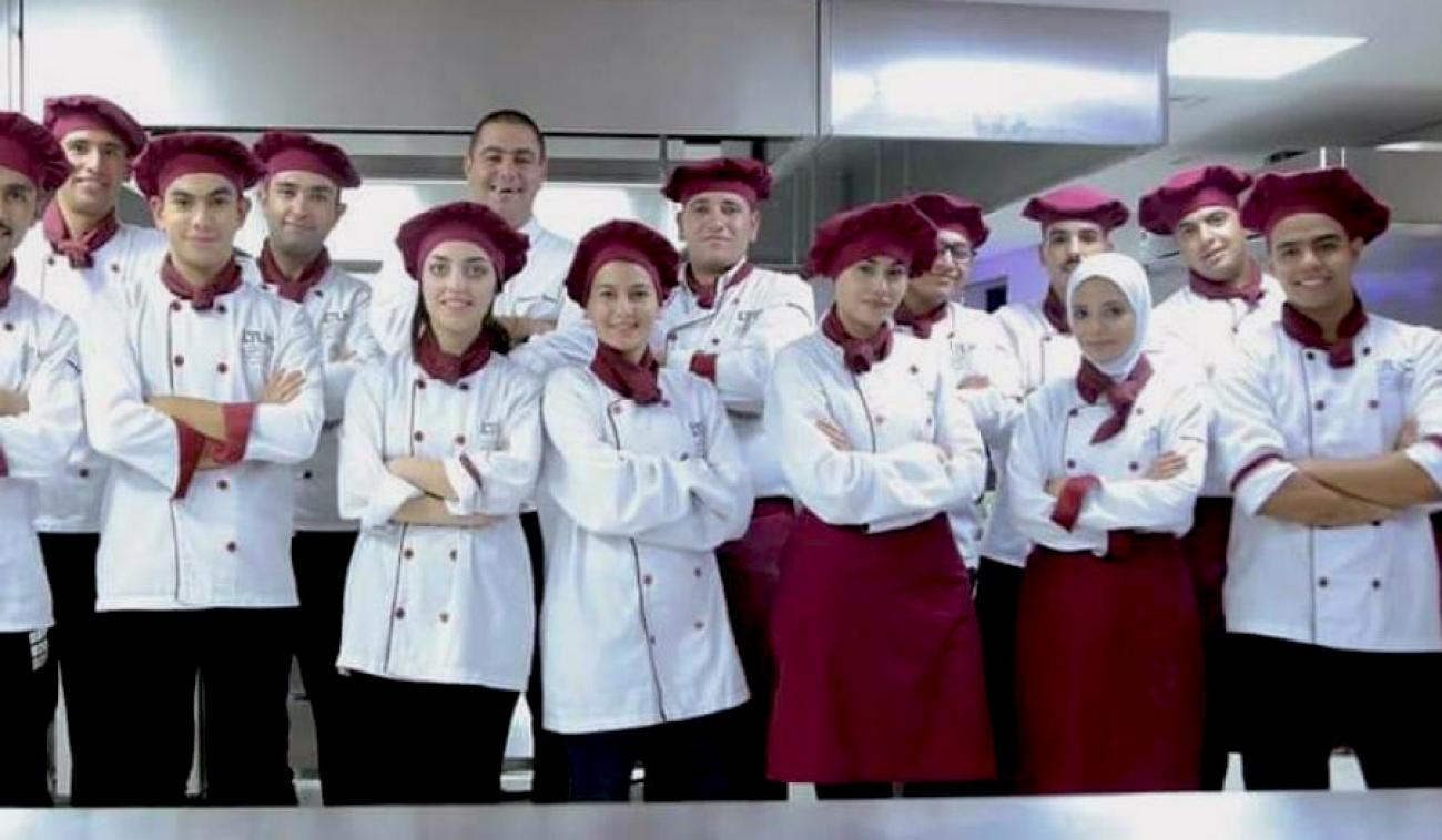 Aseel (troisième à partir de la droite) et ses camarades de classe sourient fièrement à la caméra. Ils célèbrent la fin du programme d'enseignement technique et de formation professionnelle qu’ils ont suivi. Tous portent une tenue de cuisine rouge et blanche.