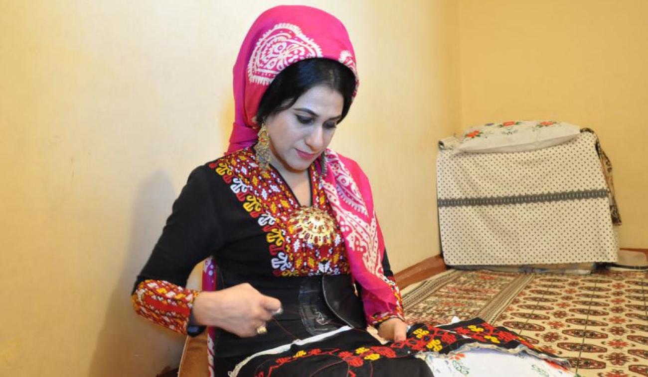 Lachyn, vêtue d’une tenue traditionnelle, est occupée à coudre un beau tissu coloré.