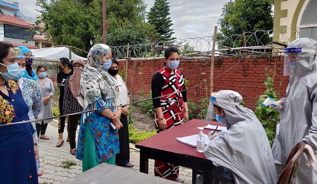 Women wait in a queue to get their temperature checked by staff at WHR's women-managed quarantine facility. 