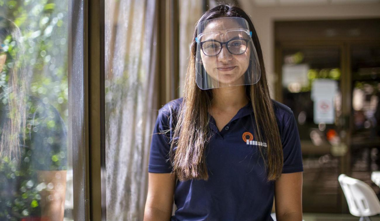 Gabriela Gamboa stands by an glass door wearing a protective face shield. 