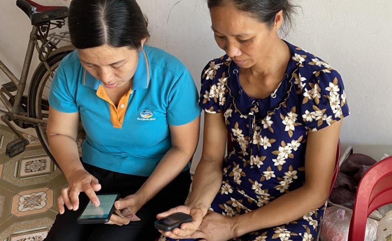 Una empleada del proveedor de servicios móviles Viettel Pay, a la izquierda de la imagen, le enseña a la Sra. Man (a la derecha de la imagen) cómo usar una herramienta de pago electrónico en su teléfono móvil para recibir asistencia social liberada por el gobierno en respuesta a la crisis de COVID-19.