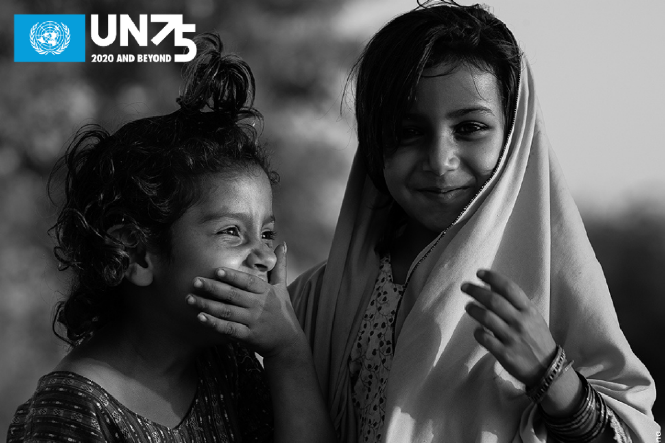 Una imagen en blanco y negro de cerca de una niña reprimiendo una risa mirando a otro lado de la cámara, mientras que otra niña sonríe con orgullo mientras mira directamente a la cámara.