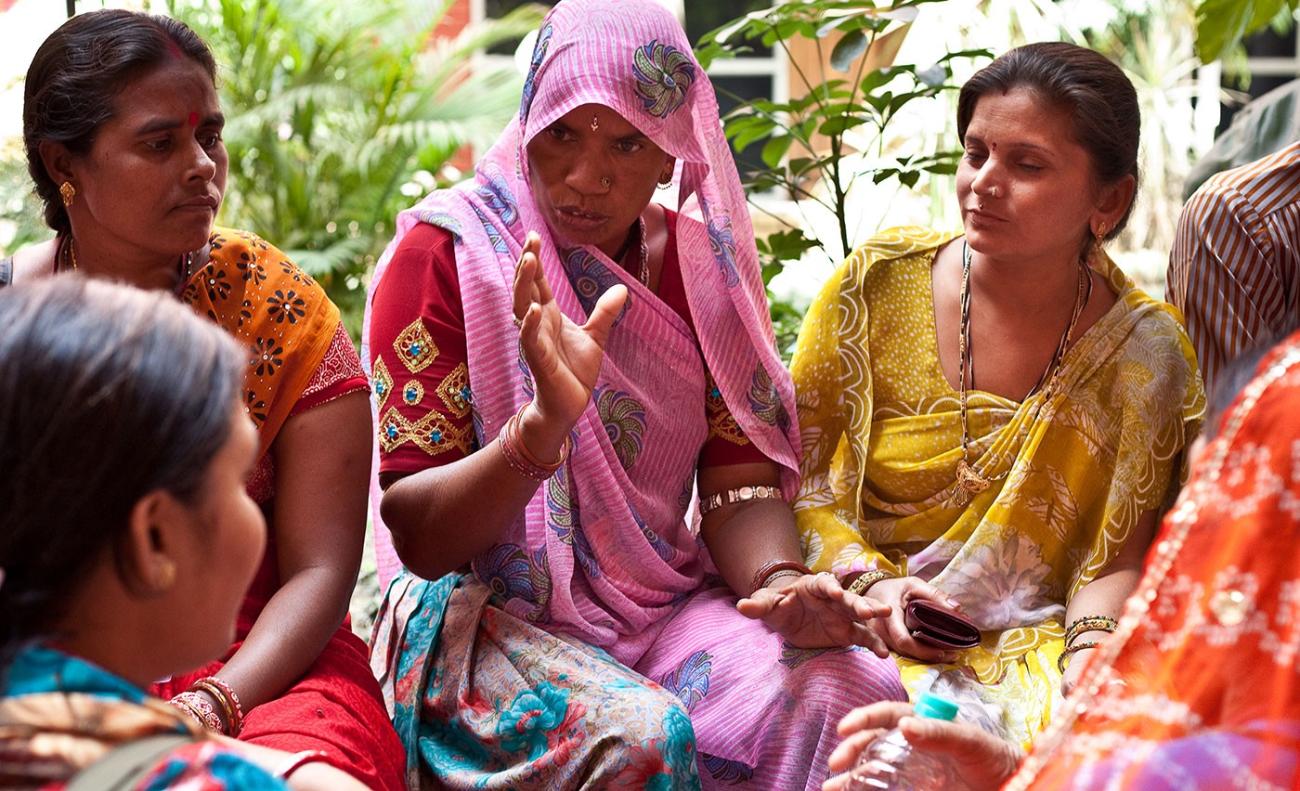 Un groupe de femmes indiennes portant des vêtements traditionnels aux couleurs vives sont assises à même le sol et discutent.