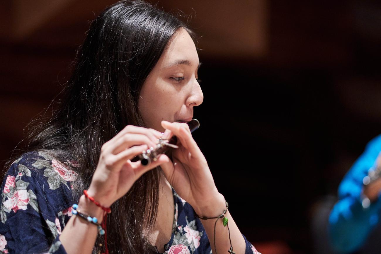 Une jeune femme joue de la flûte au sein d'un orchestre de jeunes musiciens.