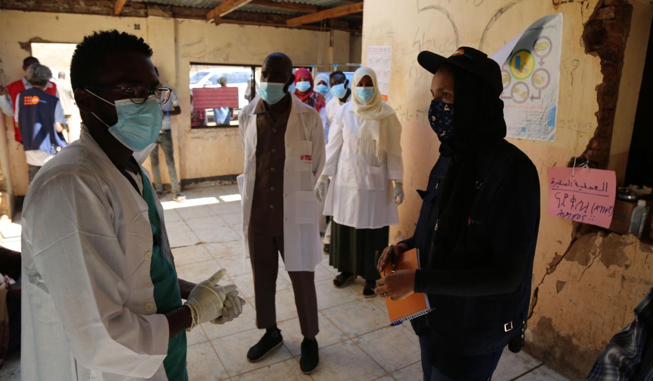El personal médico habla con el personal de la ONU en el centro médico de un campamento. Todos los presentes usan máscaras y mantienen una distancia segura entre ellos.