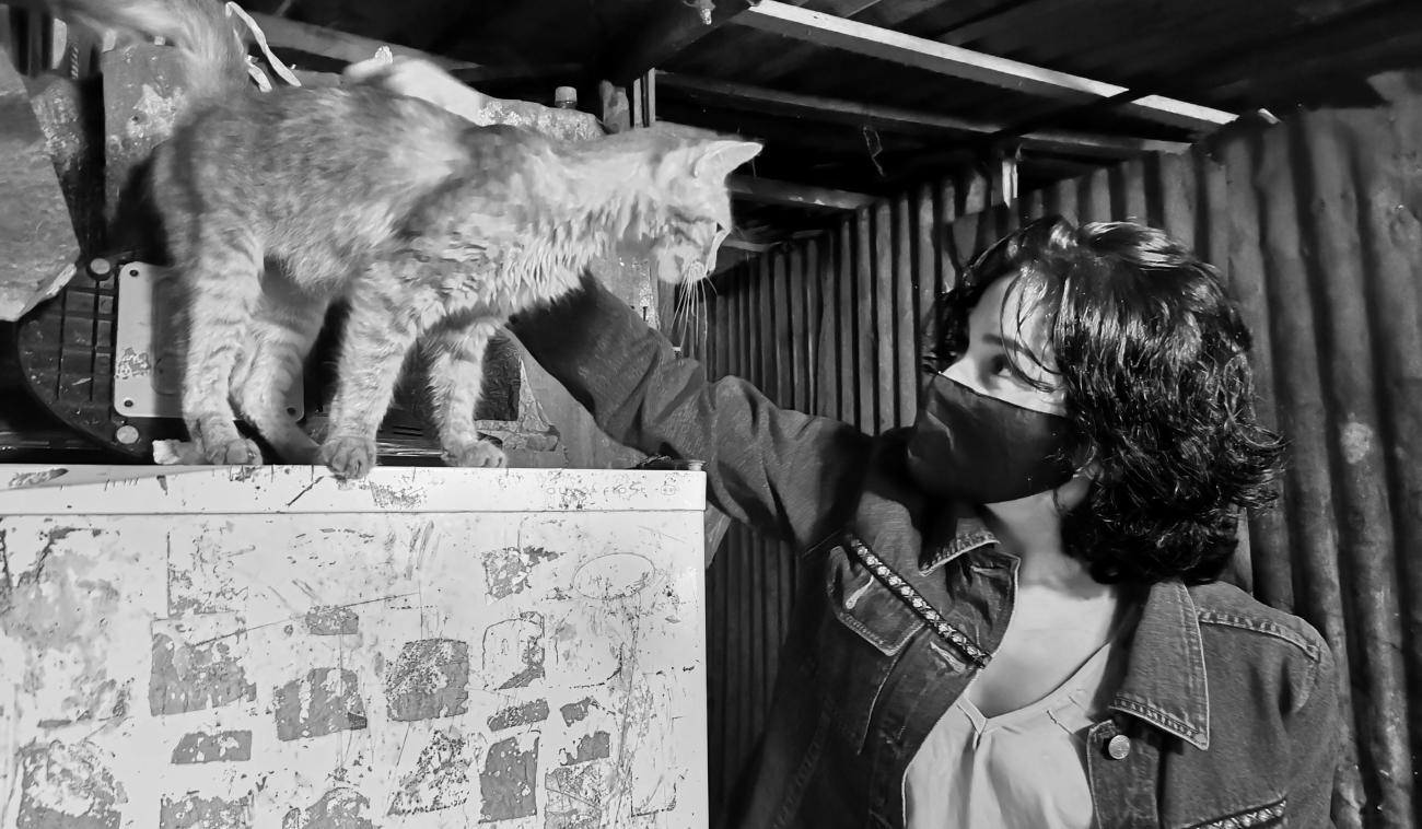 Fotografía en blanco y negro de una joven llamada Lilith, quien aparece en primer plano con mascarillas protectora y acariciando cariñosamente a un gato.