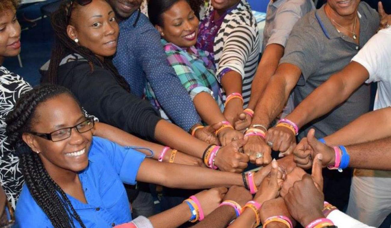 Un groupe de femmes et d'hommes, le mains jointes les unes aux autres, sourient fièrement pour montrer leur engagement solidaire pour la cause de l’élimination de la violence de genre à Trinité-et-Tobago.