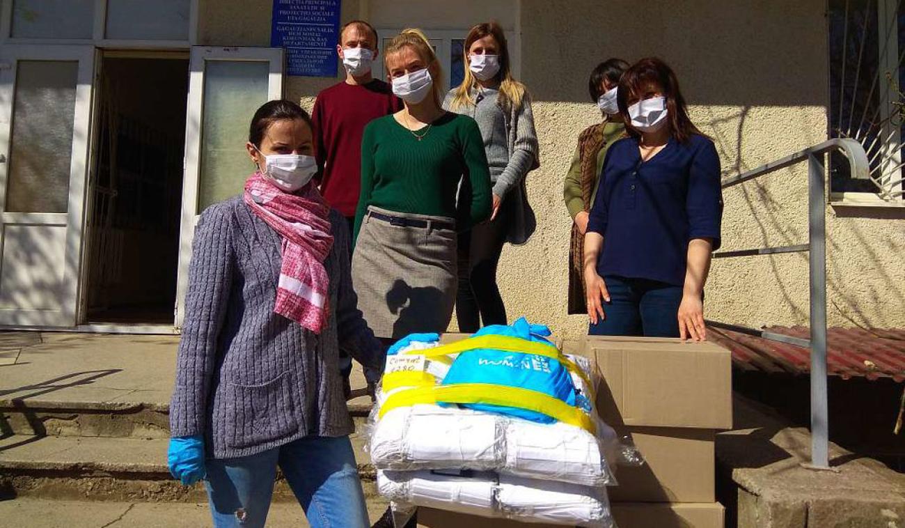 Essential workers and UN personnel stand outside by donated supplies as they wear face masks and social distance.