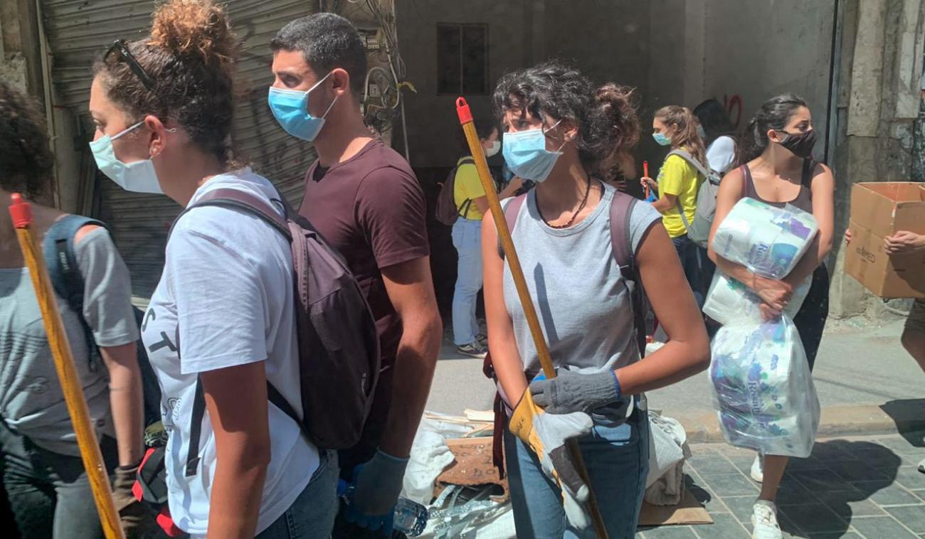 De jeunes bénévoles portant des masques de protection marchent côte à côte en portant du matériel et des fournitures.