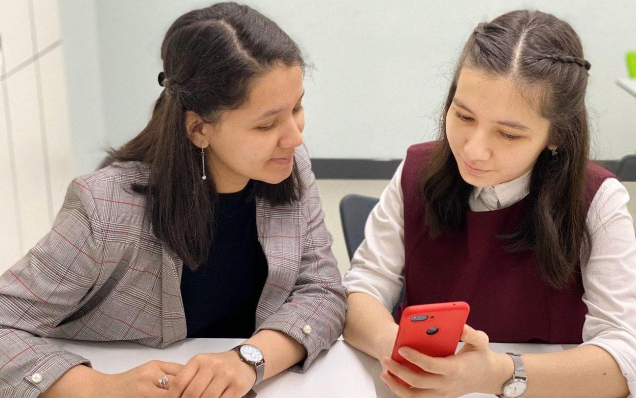 Девочка учится пользоваться программой на мобильном телефоне вместе со своим учителем. 