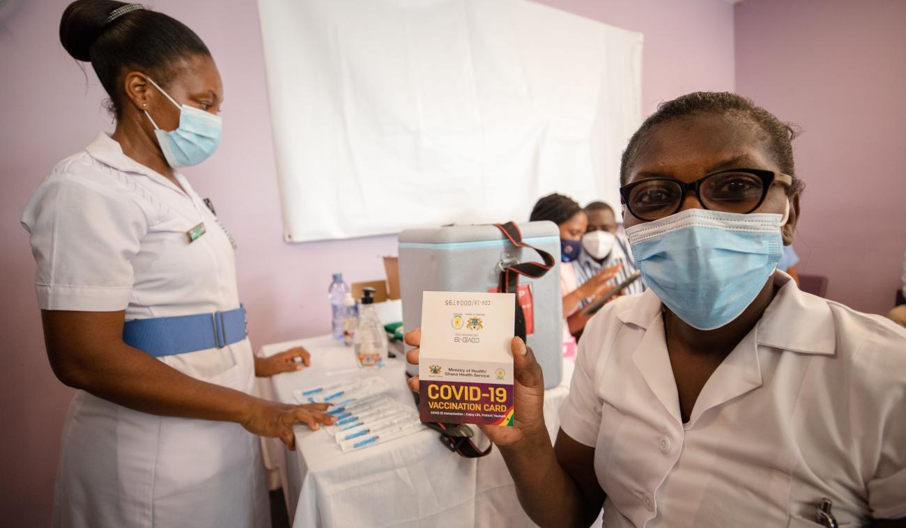 A healthcare professional at a vaccination site proudly holds up a COVID-19 vaccination card that verifies she received the vaccine.