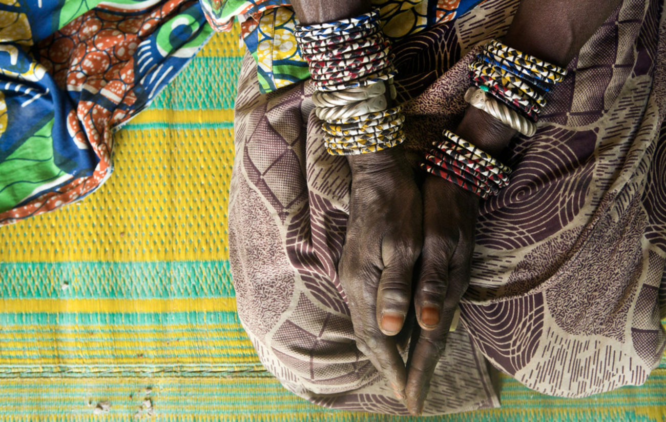 A woman's hands, with several bracelets, rest on her knees on top of a bright colored cloth.