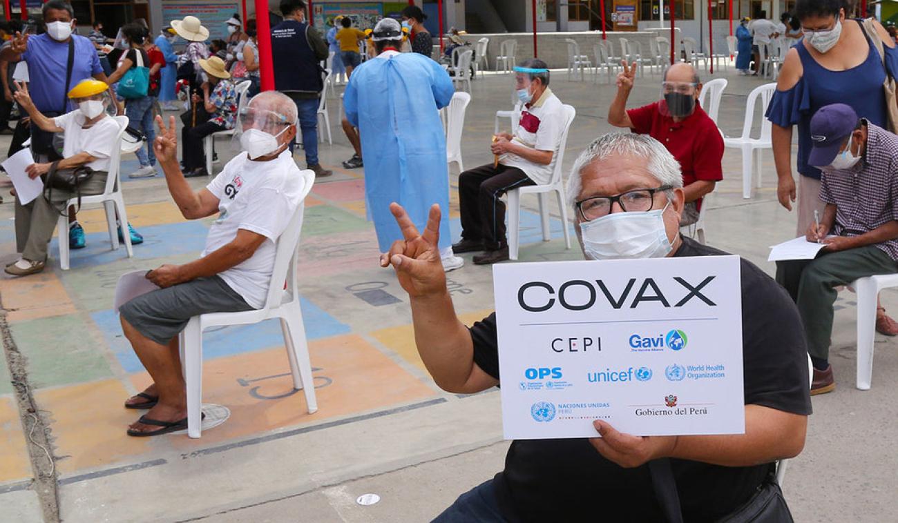 一个人举着COVAX的牌子，其他几个人对着镜头竖起大拇指并打出 "支持疫苗 "的V字手势。 