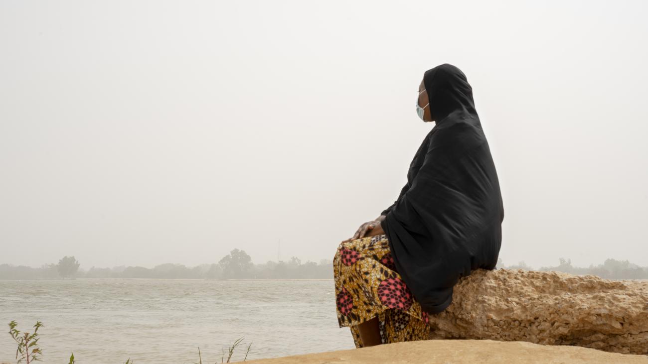 Una mujer está sentada en una roca mirando a lo lejos sobre una masa de agua.