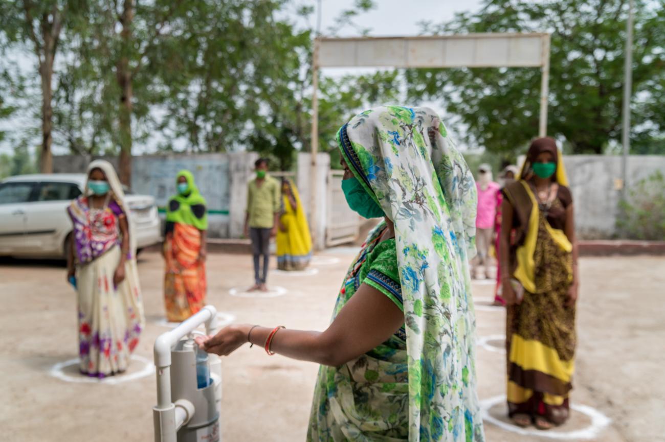 Los pacientes se distancian socialmente mientras esperan para utilizar un desinfectante de manos accionado con el pie en un centro de salud primaria en Gujarat, India