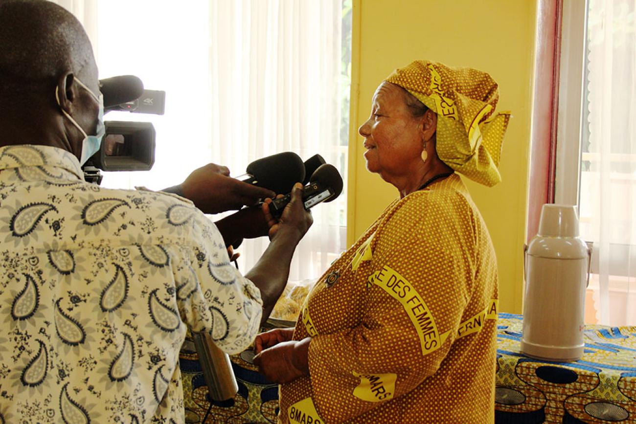 Une femme de la République centrafricaine vêtue d’une robe traditionnelle s’exprime au micro de plusieurs journalistes venus l’interviewer.