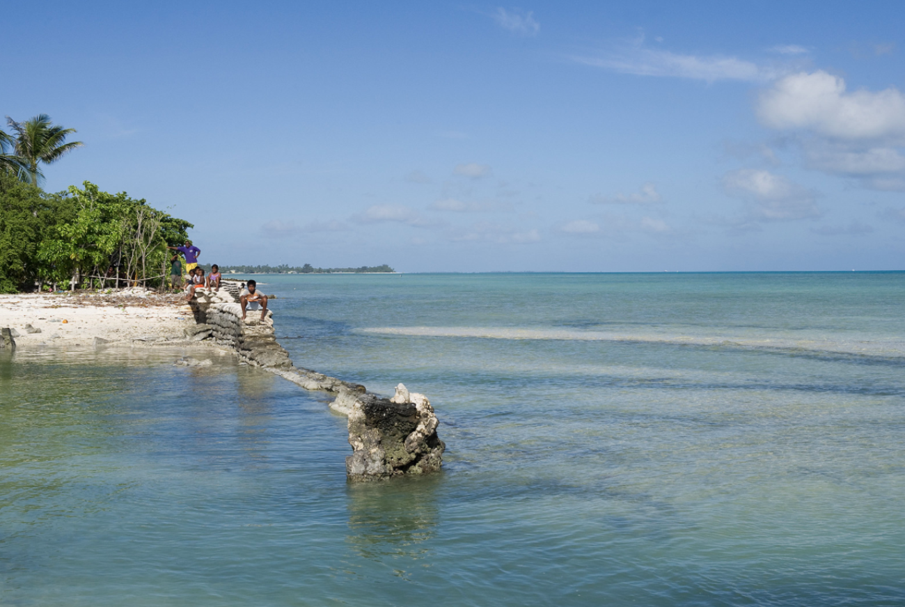 Una imagen del océano y varias personas de pie en una isla en un día soleado. 