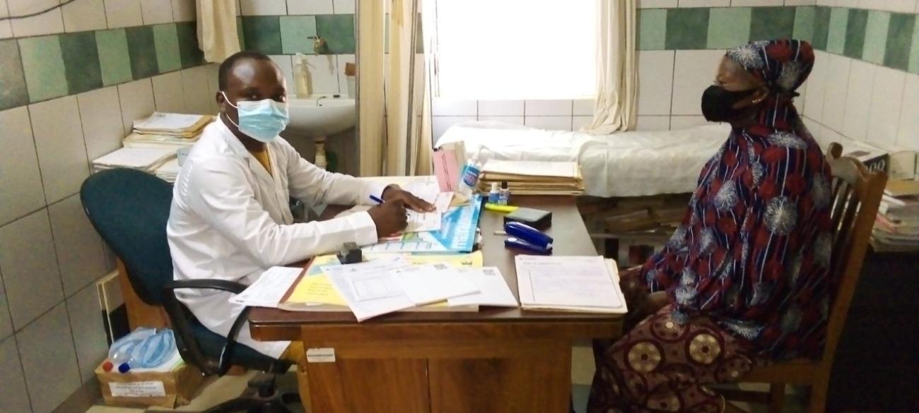 穿着白大卦的医生（左）为坐在桌子另一边的患者看诊。