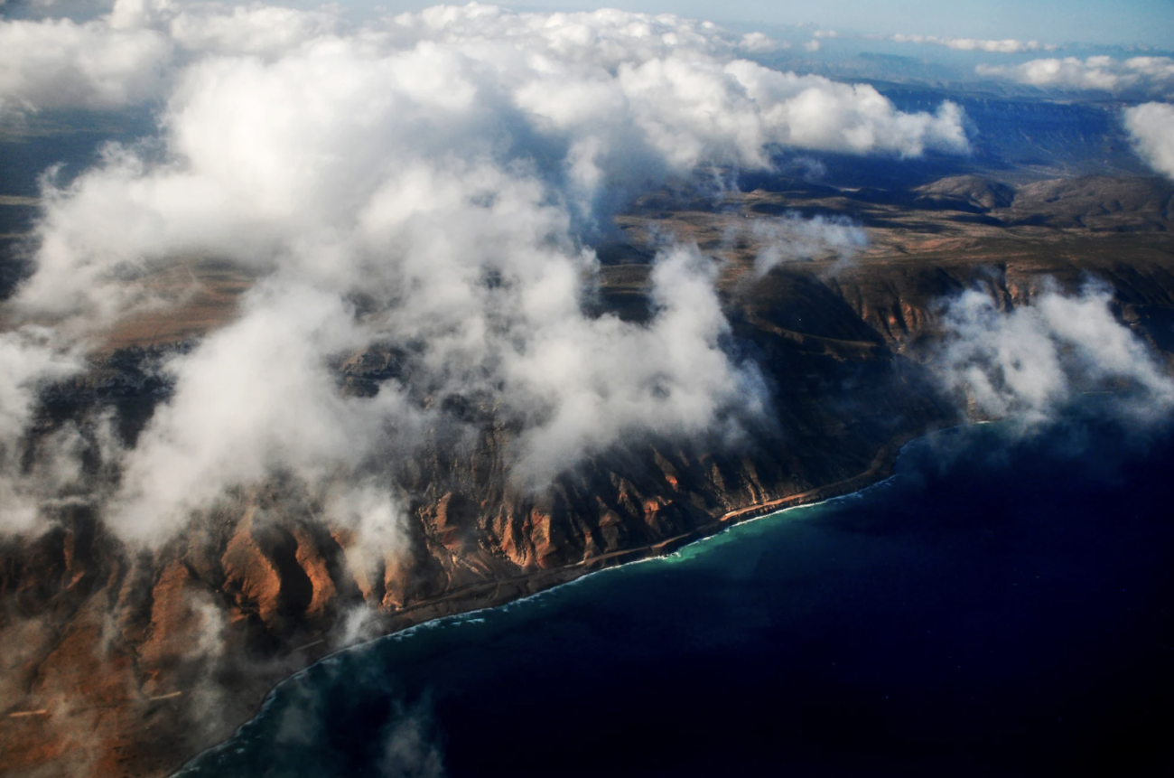 An areal shot of a coastline with clouds in the sky.