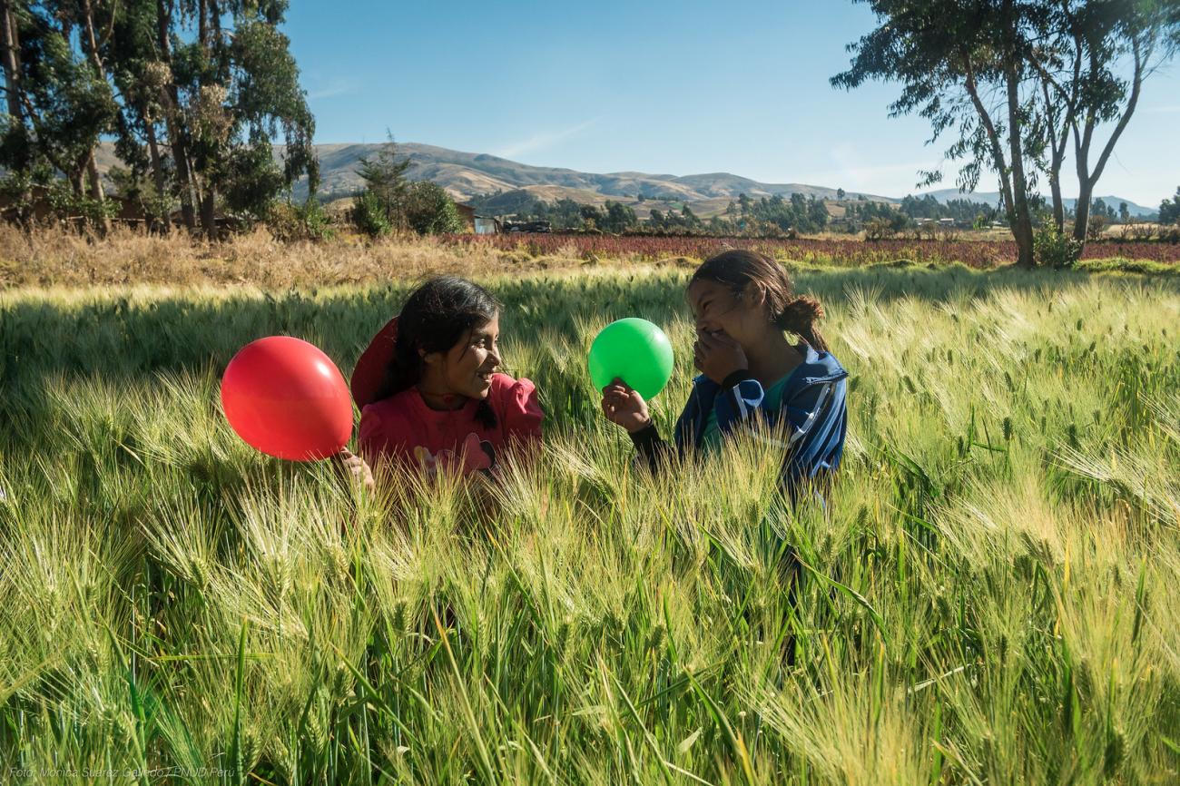 Two girls in a field play with a green and red balloon. 