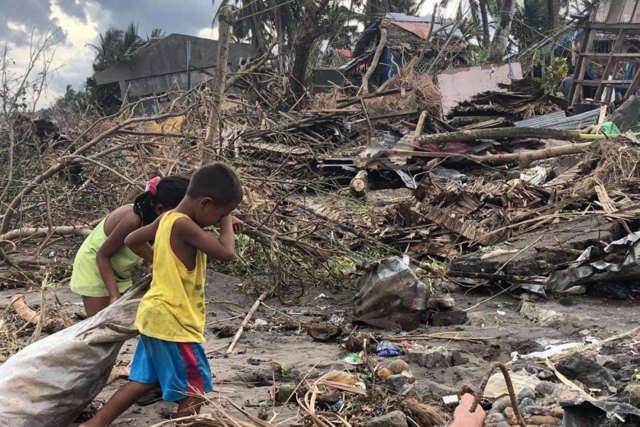 Two children walk with a bag in their hands near debris of a home.