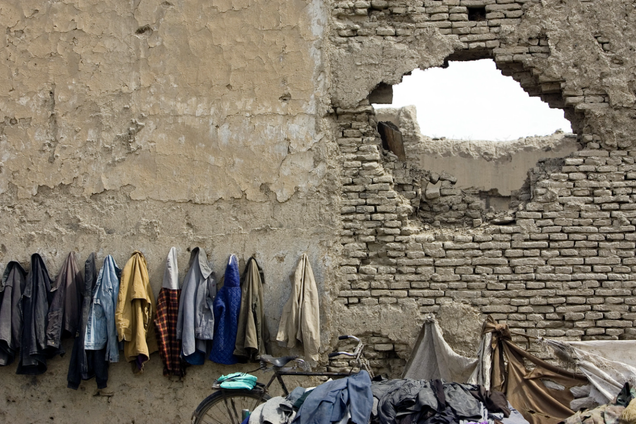 Several coats hanging outside a building with a a large hole to the right of the coats. 