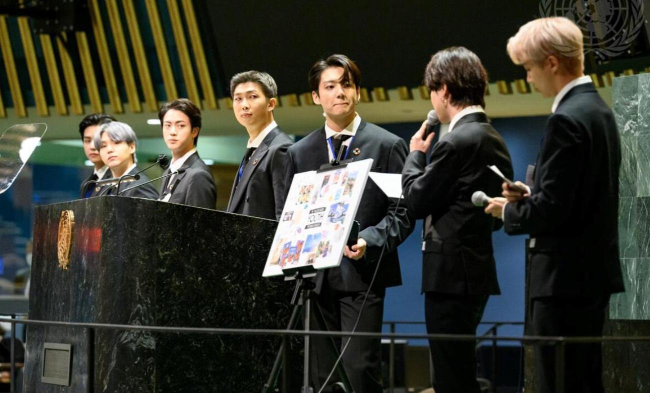 سبعة أعضاء من فرقة موسيقى البوب الكورية BTS يرتدون بدلات ويتحدثون في الجمعية العامة.