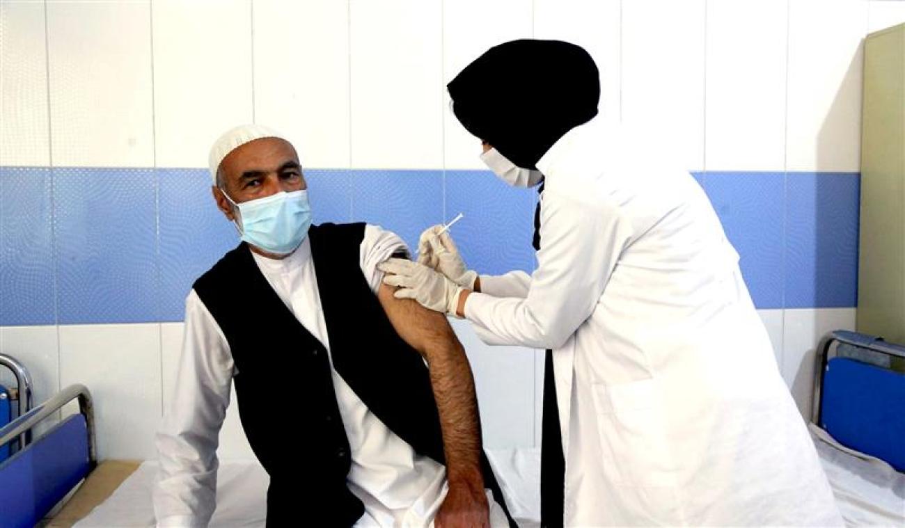 رجل جالس يتلقى اللقاح من قبل امرأة تقف في عيادة الطبيب.