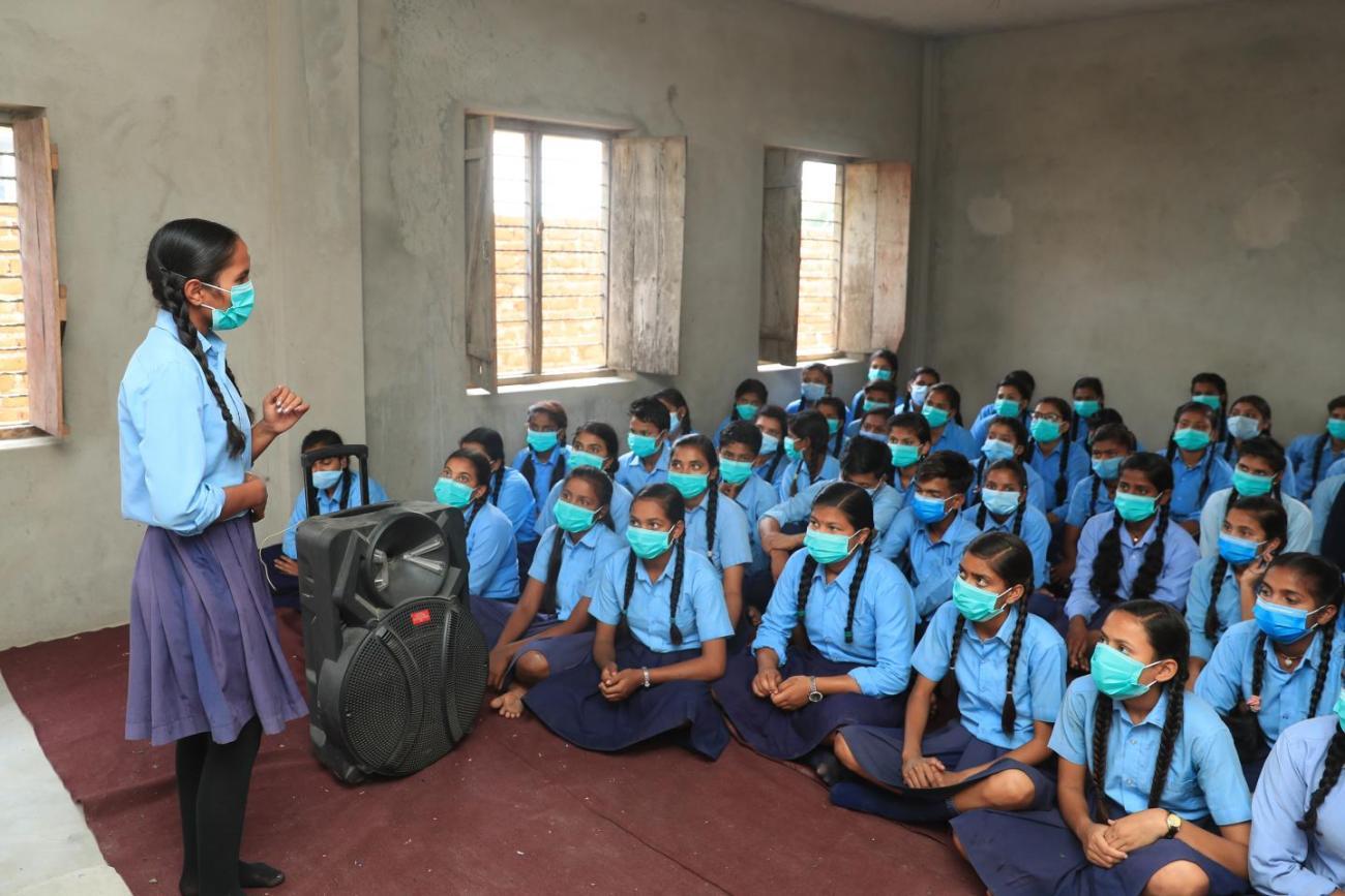 فتاة تقف أمام صف مليء بالطالبات اللواتي يلبسن الزي المدرسي.