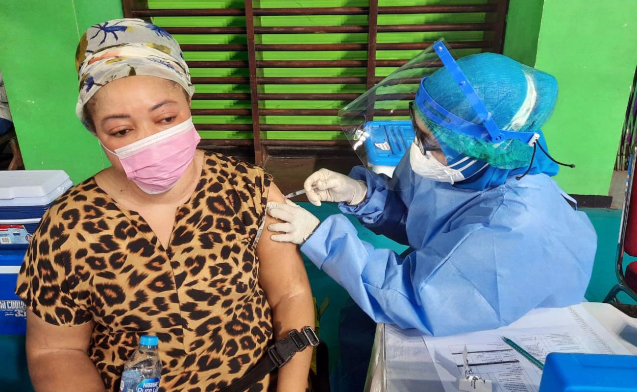 A healthcare professional gives a refugee woman, wearing a mask, her first jab of the COVID-19 vaccine.