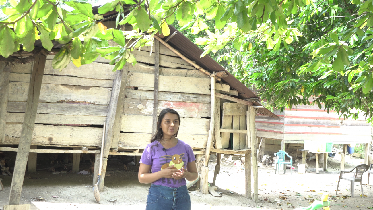 A woman stands in front of a house made of wood planks. 
