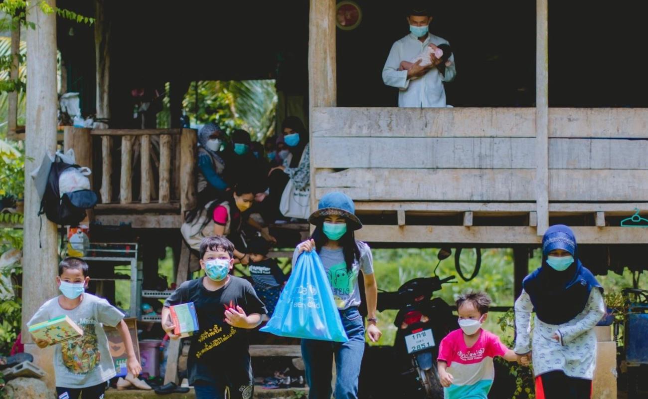 Families and children wearing mask outside a home. Five children proudly walk away from the home and towards the camera holding supplies provided by UNICEF.