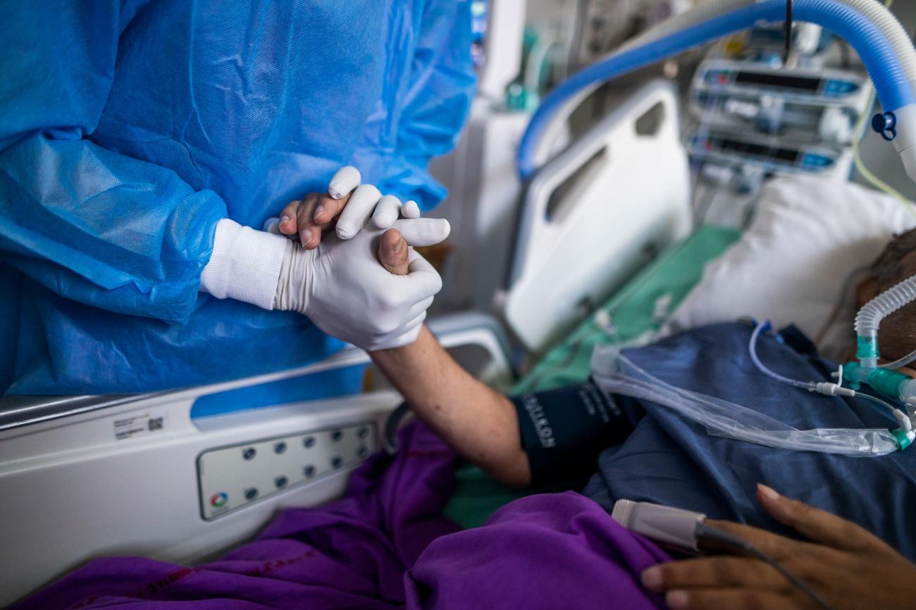 A patient and a medical professional hold hands as the person lies in a hospital bed. 