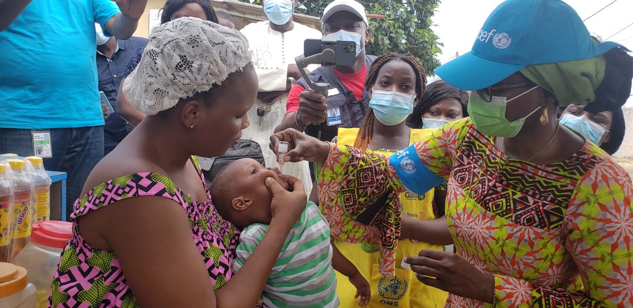 يُعطى طفل صغير لقاح شلل الأطفال عن طريق قطرات في فمه بينما تمسكه أمه.