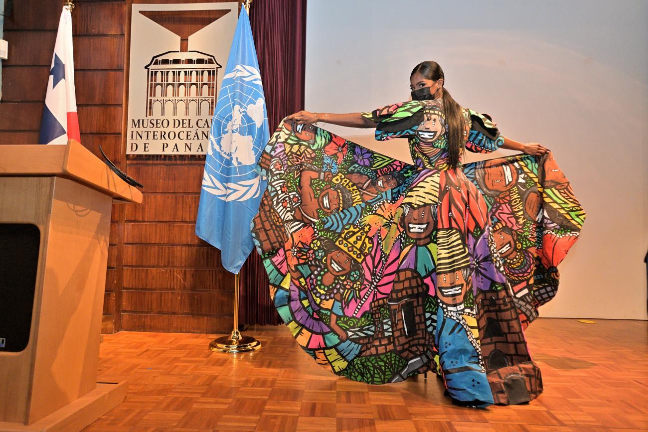 A woman stands on a stage showing a unique pattern on her colorful dress. 