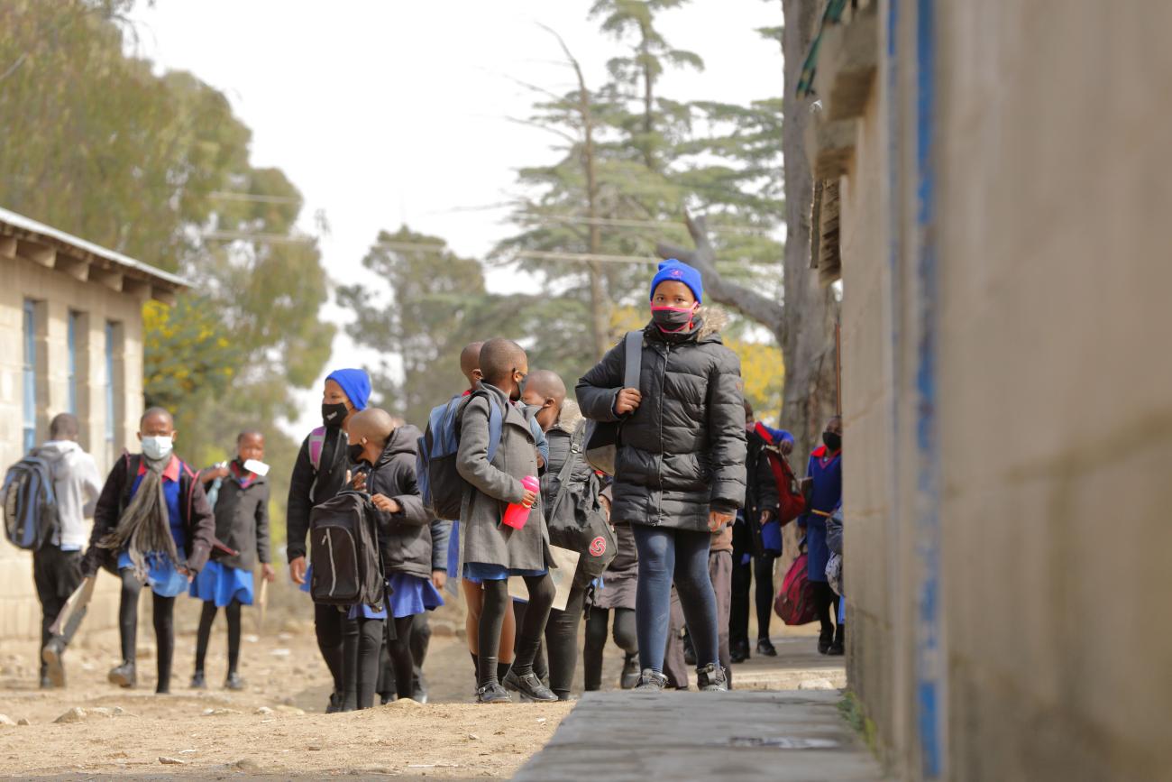 Группа детей школьного возраста в масках на лицах выходят из здания школы. 